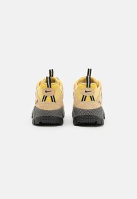 Les baskets Nike Air présentent une tige jaune et beige, une semelle texturée noire et des accents noirs contrastants. Le design comprend deux languettes de tirage.
