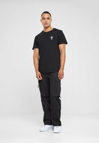 Sort bomulds T-shirt med et lille hvidt logo på brystet, parret med sorte cargo bukser med flere lommer og lynlåse, afsluttet med hvide sneakers.