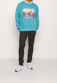 Sweat-shirt turquoise avec un graphisme "WILD RIDE", coupe décontractée. Pantalon noir ajust é et baskets blanches avec des accents bleus. Tenue décontractée.