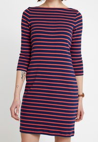 Laivastonsininen ja punaraitainen mekko, jossa on kolme neljäsosaa hihat, veneen kaula-aukko ja rento istuvuus. Valmistettu pehmeästä, venyvästä kankaasta.