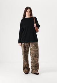 Black long-sleeve top with a boxy fit, paired with leopard print wide-leg trousers and black platform shoes; holding a brown crossbody bag.