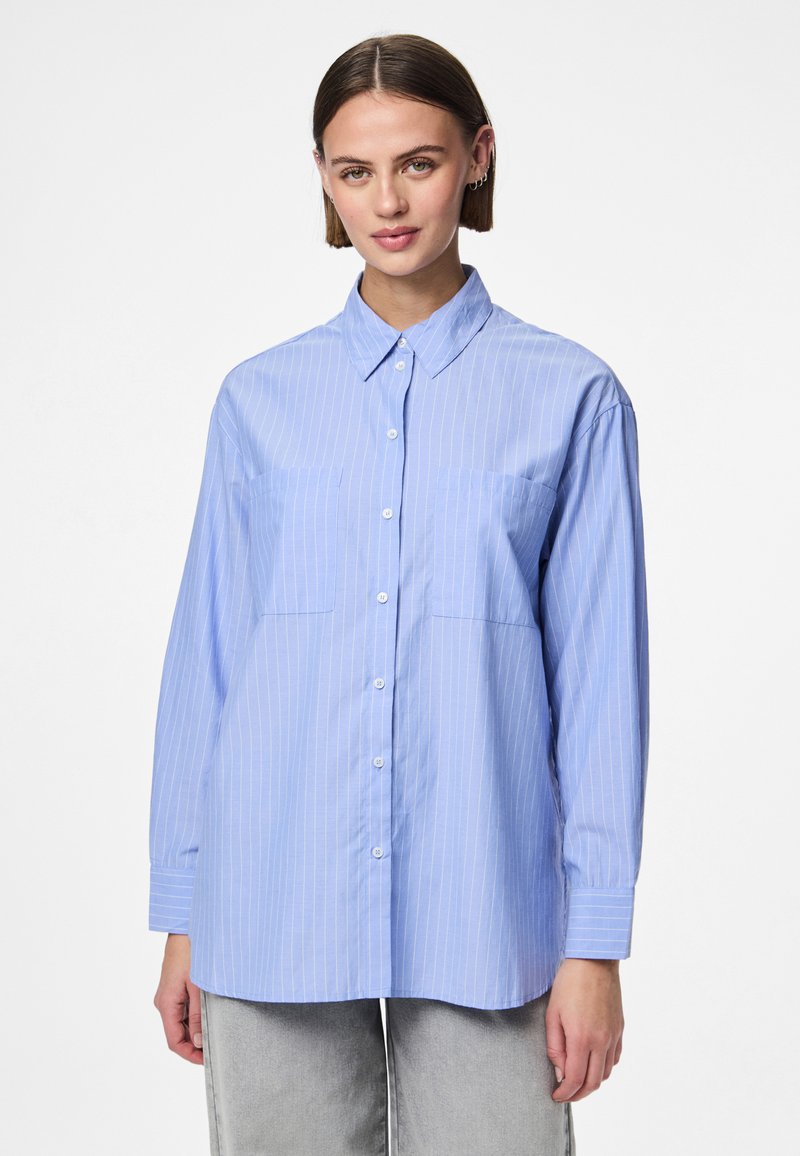 Vaaleansininen raidallinen nappipaita, jossa on pitkät hihat, terävä kaulus, kaksi rintataskua ja väljä istuvuus. Puuvillakangas, jossa on sileä pinta.