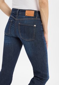 Dunkelblaue Denim-Jeans im Slim-Fit, mit einem hellbraunen Lederaufnäher am hinteren Bund und Kontrastnähten.