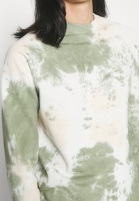 Sudadera tie-dye en verde claro y crema con cuello acanalado y textura suave, que presenta un corte relajado y mangas raglán.