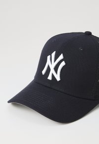 Marineblå baseballcap med en strukturert front, hvit brodert logo, mesh sidepaneler og en buet skygge. Teksturerte stofffinish.