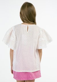 Vit blus med rosa och orange prickar, spetsdetaljer på vida ärmar, knäppning på baksidan, tillsammans med en rosa kjol.