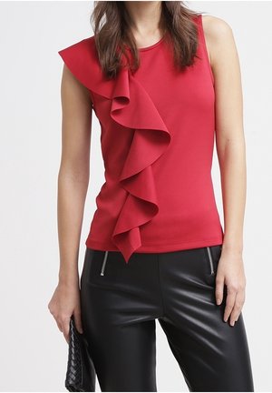 Sleeveless red top with large ruffle detail down front paired with black leather pants with front zipper pockets, holding black clutch.