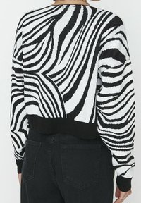 Svart- och vitrandig tröja med en strukturerad stickad mönster, kort design och svart ribbad fåll, tillsammans med mörka jeans.