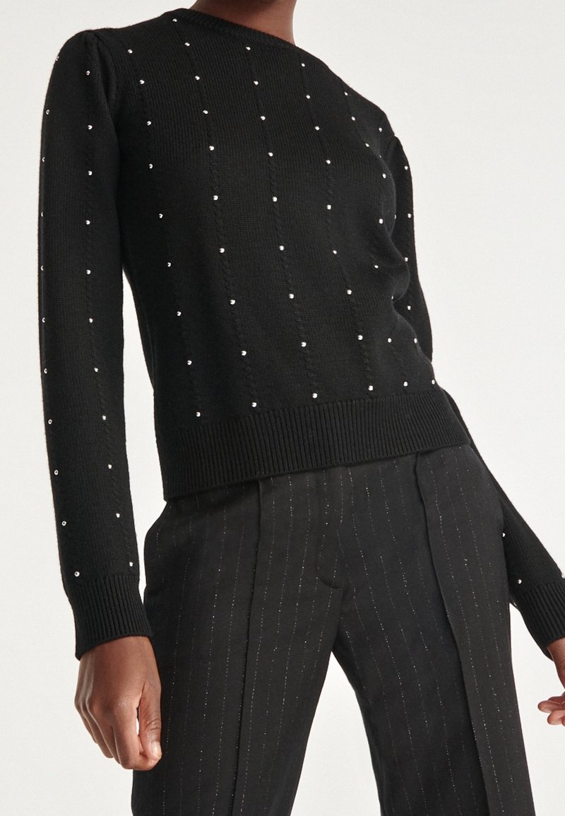Schwarzer Strickpullover mit Puffärmeln, strukturiert mit vertikalen Reihen von kleinen silbernen Verzierungen; tailliertes Design mit geripptem Saum.