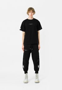 Camiseta oversized negra con un parche y joggers negros que presentan acentos de plumas texturizadas, combinados con botas blancas de cordones.