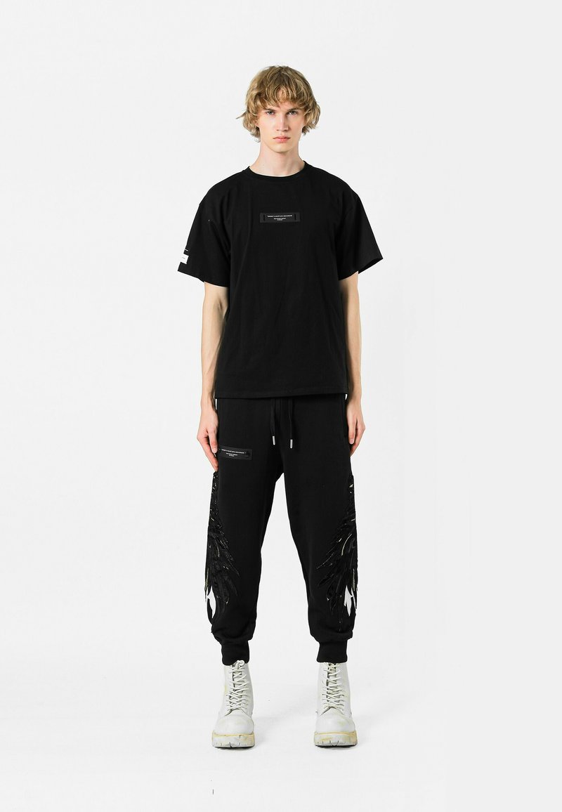 Camiseta oversized negra con un parche y joggers negros que presentan acentos de plumas texturizadas, combinados con botas blancas de cordones.