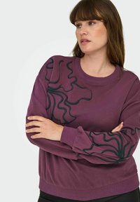 Sudadera púrpura con patrón abstracto negro en las mangas, puños y dobladillo acanalados, cuello redondo y textura de tela suave.