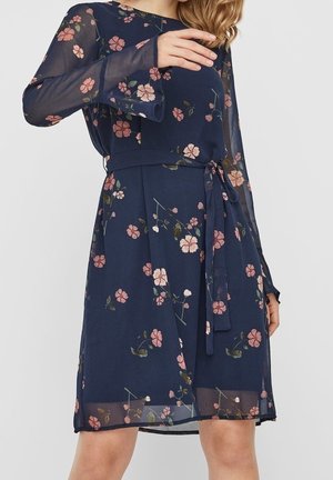 Tmavě modré květované šaty s dlouhými průsvitnými rukávy, páskem na zavazování v pase a splývavým střihem se vzorem růžových a bílých květů.