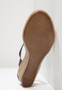 Sandale compensée avec semelle en caoutchouc marron texturé, semelle intercalaire en jute tissée, bride noire à la cheville, taille 37, marque "rieker" embossée sur la semelle.