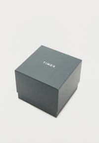 Caja de embalaje de Timex, cuadrada, de cartón verde oscuro con acabado mate, con el logotipo de la marca en relieve en blanco en la parte superior.