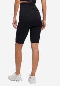 Pantaloni shorts neri realizzati in tessuto testurizzato, con un'ampia vita elasticizzata e lunghezza fino a metà coscia. Indossati con scarpe da ginnastica bianche.