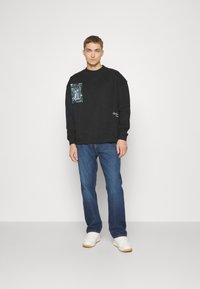 Zwarte sweatshirt met een zak en een grafische print, gecombineerd met blauwe denim jeans en witte sneakers. Eenvoudig en ontspannen pasvorm ontwerp.