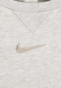 Sivý sveter vyrobený z jemného materiálu, s rebrovaným golierom a malým, vyšitým béžovým logom Nike na hrudi.