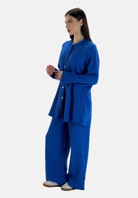 Blusa azul de botones con cuello y mangas largas, acompañada de pantalones de pierna ancha a juego. Fabricada en un tejido texturizado, presenta un diseño relajado.