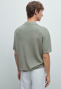 Polo a maniche corte di colore verde oliva chiaro, texture a maglia, con colletto classico e polsini a costine, visto da dietro.