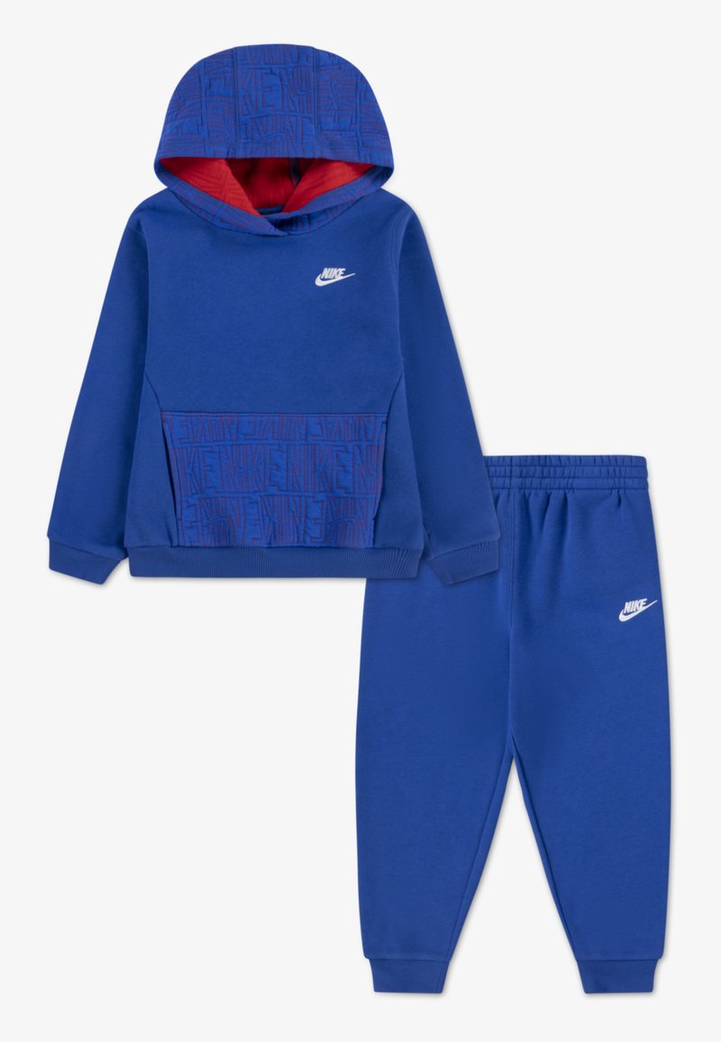 Kék Nike kapucnis pulóver piros béléssel, mintás elülső zsebbel. Hozzáillő kék melegítőnadrág, elasztikus derékkal és logóval.