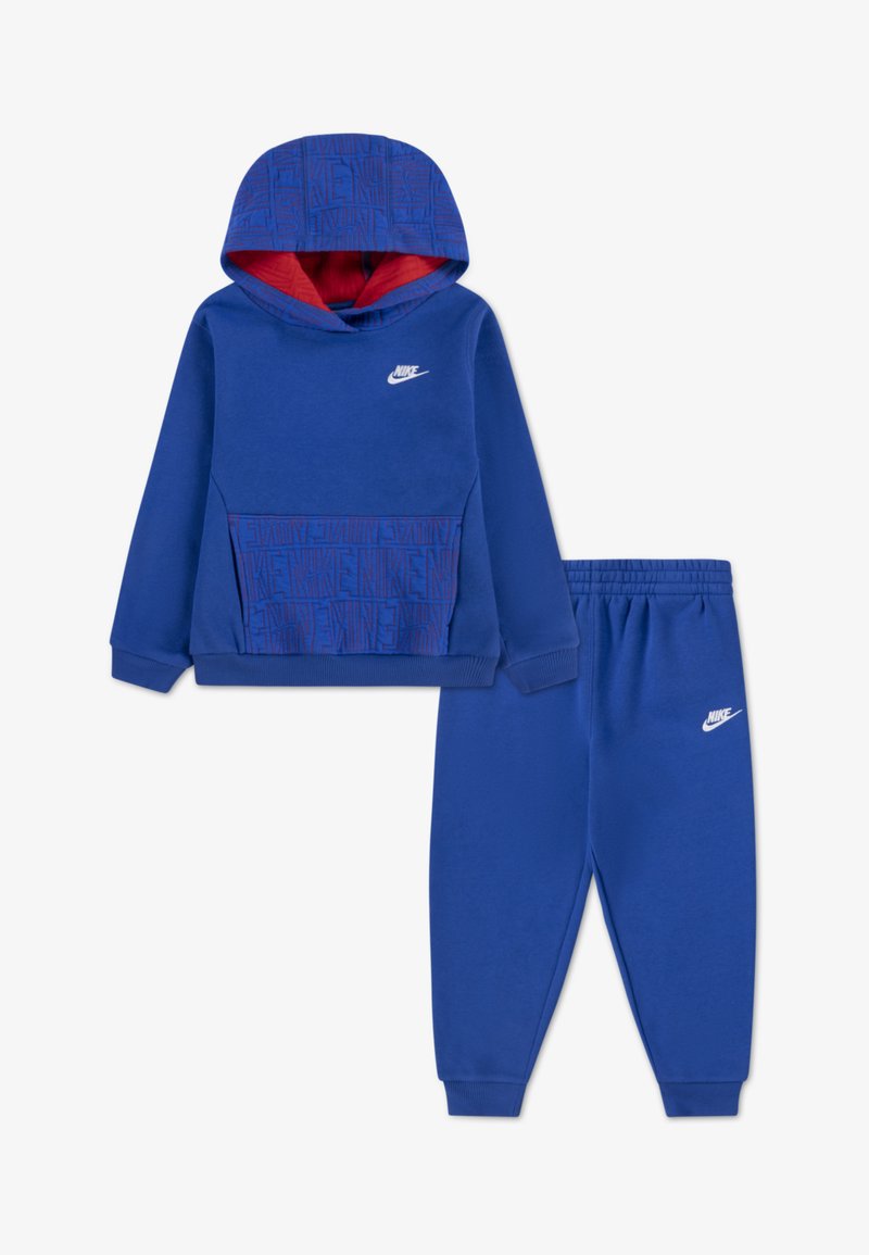 Kék Nike kapucnis pulóver piros béléssel, mintás elülső zsebbel. Hozzáillő kék melegítőnadrág, elasztikus derékkal és logóval.