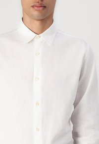 Camicia bianca con bottoni in tessuto leggero, dotata di colletto classico, bottoni perlacei e una finitura testurizzata.