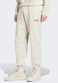 Cream-colored sweatpants with an elastic waistband, side pockets, and ribbed cuffs. Notable logo on the left thigh.