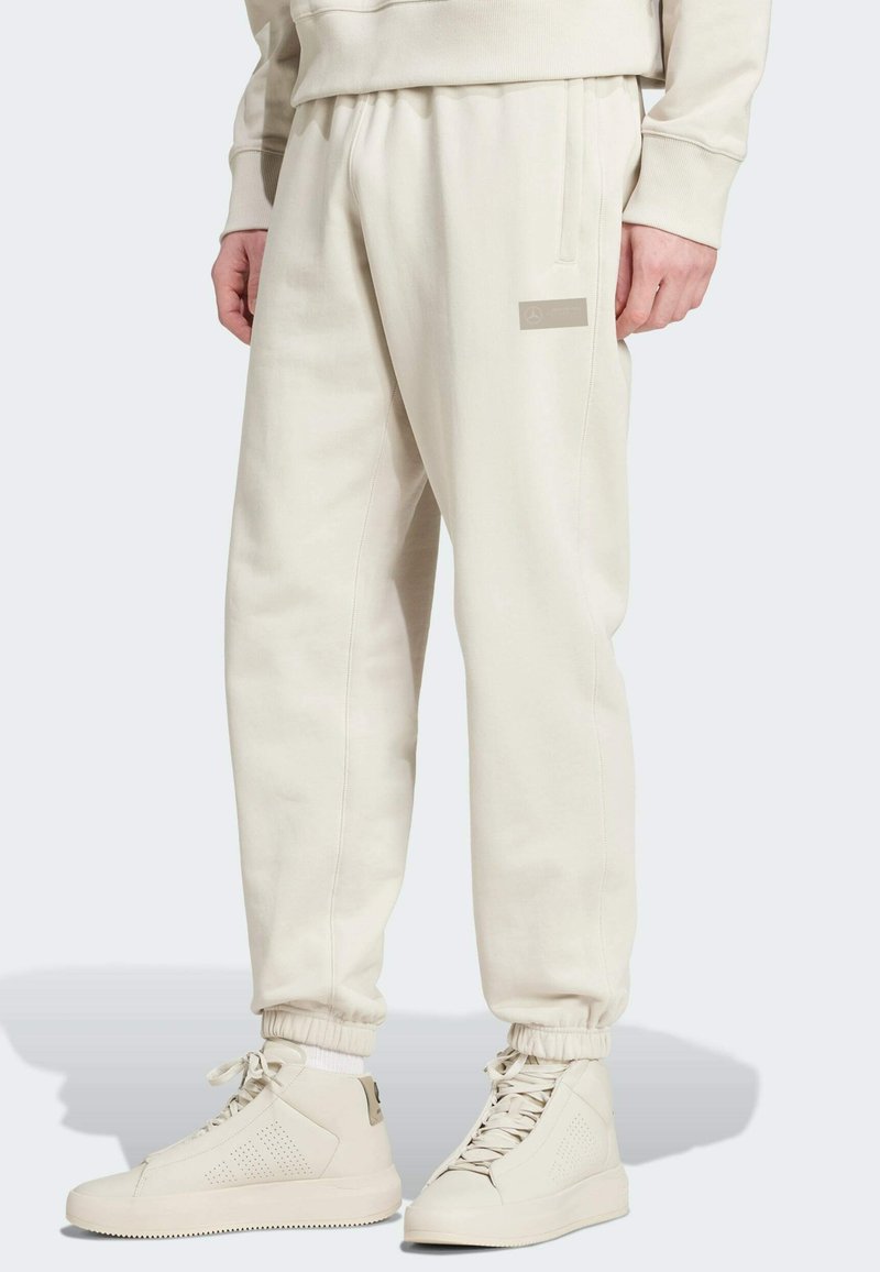 Cream-colored sweatpants with an elastic waistband, side pockets, and ribbed cuffs. Notable logo on the left thigh.