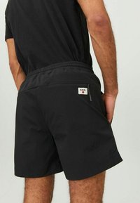 Schwarze Shorts aus leichtem Material mit elastischem Bund, ausgestattet mit einer Gesäßtasche und einem Etikett mit dem Design "R.D.D.".