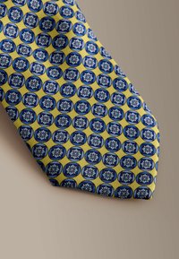 Corbata con un patrón circular repetitivo en azul con motivos florales, sobre un fondo amarillo; tela suave, punta puntiaguda.