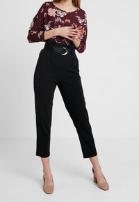 Bordeaux bloemenblouse met driekwartmouwen, gecombineerd met zwarte hoge taillebroeken met een grote zilveren ceintuur. Beige hakken.