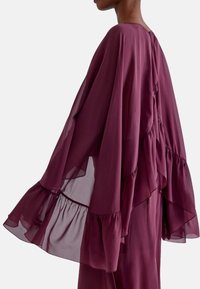 Abito fluente color bordeaux con maniche a strati e arricciate e scollatura alta. Realizzato in tessuto leggero e trasparente con una texture liscia.