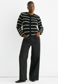 Black and white striped cardigan with a soft texture, button closure, and long sleeves, paired with wide-leg black jeans and black shoes.