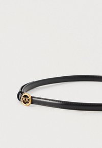 Melna ādas josta ar mazu zelta apaļu sprādzi, uz kuras attēloti divi spārnoti bišu motīvi, izstādīta uz gaiša fona.