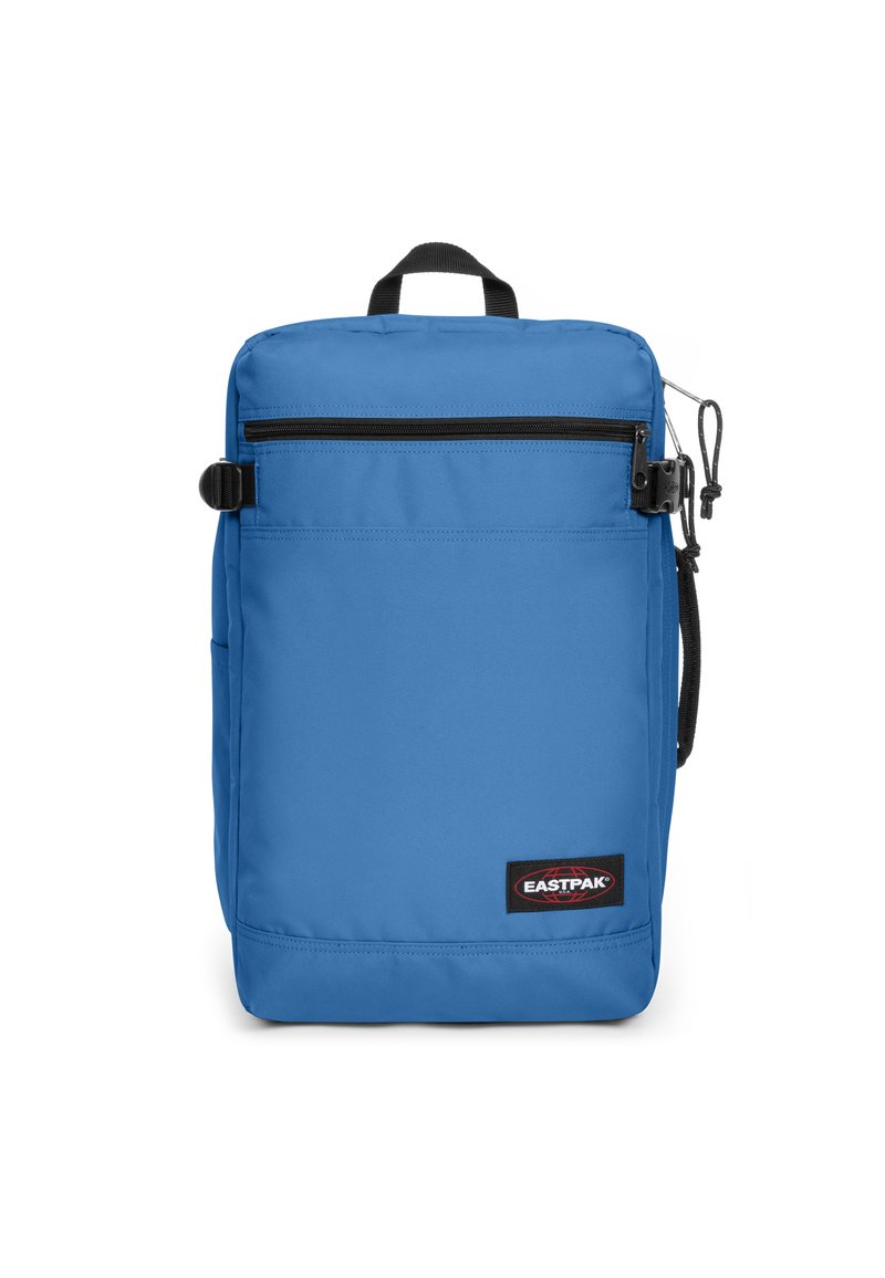 Mochila de poliéster azul con un asa en la parte superior, bolsillo frontal con cremallera, correa de hombro ajustable y un emblema visible. Textura suave.