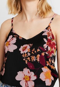 Camisole noire à motifs floraux avec un décolleté en V profond, des bretelles fines, et un mélange de fleurs roses, orange et rouge foncé sur une texture lisse.