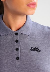 Polo gris avec un tissu texturé, un col classique, quatre boutons noirs et un petit logo brodé sur la poitrine à gauche.