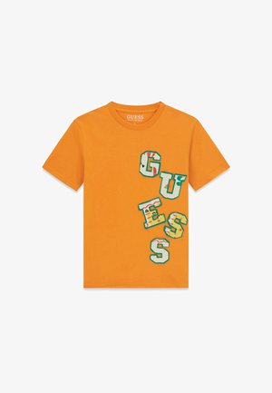 Pomarańczowy T-shirt z krótkim rękawem z wielokolorowymi literami naszywkami tworzącymi napis "GUESS" ukośnie po prawej stronie z przodu.