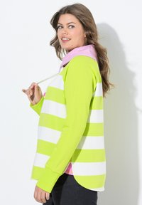 Maglietta a maniche lunghe verde e bianca a righe con cappuccio rosa e cordoncino. Presenta un orlo curvo e spacchi laterali. Materiale morbido.