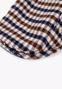 Cappello di lana con un motivo a quadri blu, marrone e crema, caratterizzato da una consistenza morbida e pelosa e da un design con visiera arrotondata.