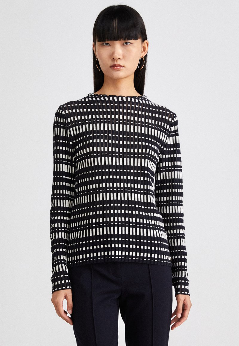 Schwarz-weißer Langarmoberteil mit Karomuster, rundem Ausschnitt, gerippter Textur und tailliertem Schnitt. Kombiniert mit dunklen Hosen.