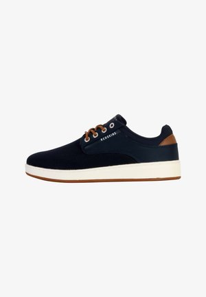 Baskets en toile navy avec des accents en cuir marron, semelle en caoutchouc blanc, bout rond, design à lacets et marquage "REDSKINS" sur le côté.