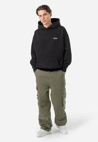 Black hooded sweatshirt with front pocket and white logo, paired with olive green cargo pants featuring multiple pockets and a loose fit.