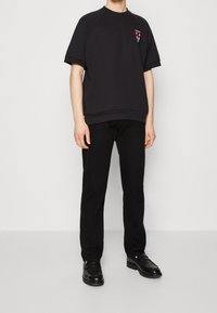 Svart bomullsoverdimensionerad t-shirt med korta ärmar och ribbstickad rundhals. Har en grafisk design på bröstet. Tillsammans med svarta byxor och skor.