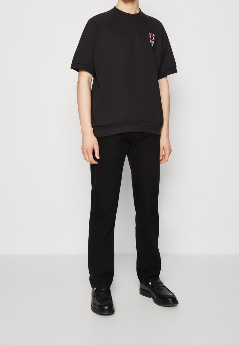 Svart bomullsoverdimensionerad t-shirt med korta ärmar och ribbstickad rundhals. Har en grafisk design på bröstet. Tillsammans med svarta byxor och skor.