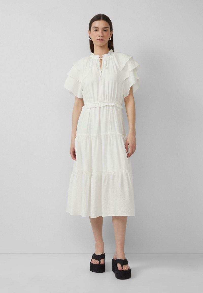 Witte gelaagde jurk met ruffle-mouwen, elastische tailleband en een keyhole-halslijn. Gekoord met zwarte platform sandaaltjes. Effen, lichtgewicht stof.