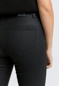 Svarta denimjeans med sydda fickor, midjehöjd och en diskret märkesetikett baktill. Slät textur med en skräddarsydd passform.