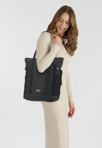Borsa tote in nylon nero con tasche laterali in rete, spallacci imbottiti e chiusure con fibbia. Presenta un design strutturato con una texture liscia.