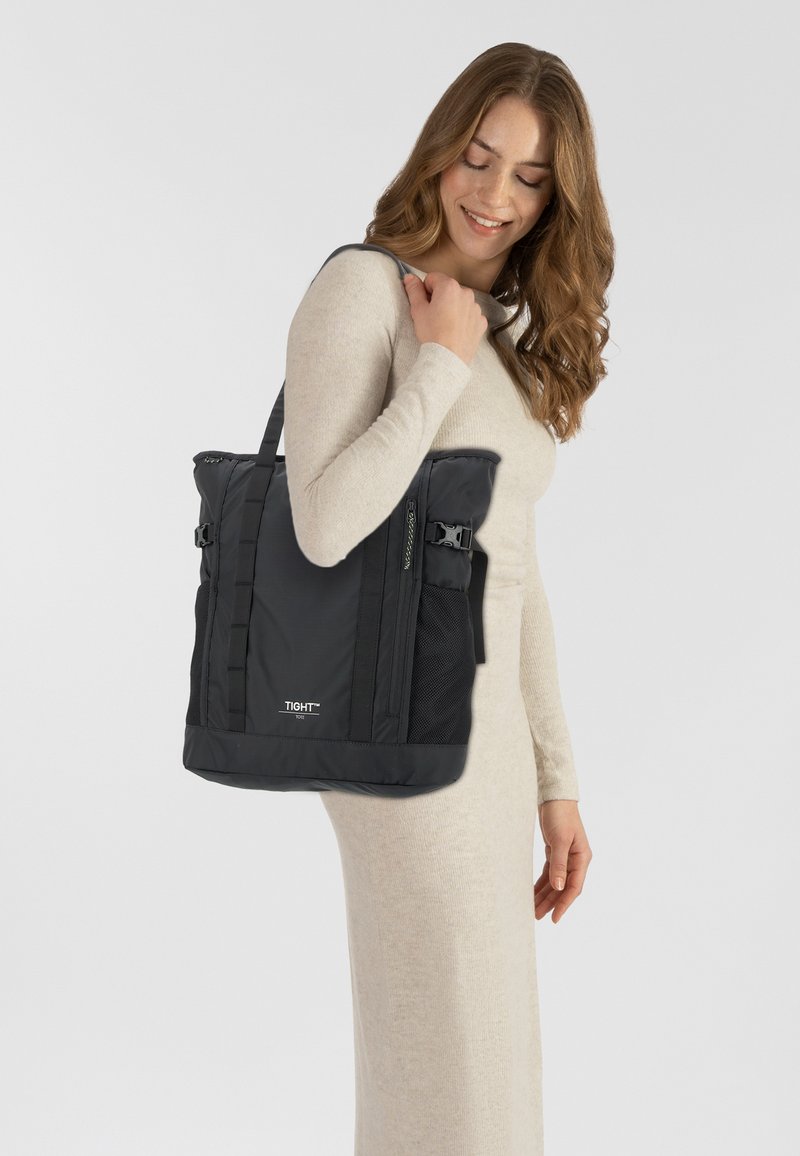 Borsa tote in nylon nero con tasche laterali in rete, spallacci imbottiti e chiusure con fibbia. Presenta un design strutturato con una texture liscia.